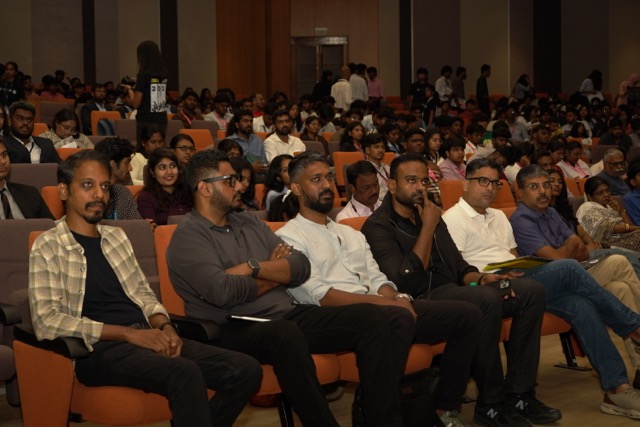 The auditorium audience, with panelists including Raja T M seated in the front row
